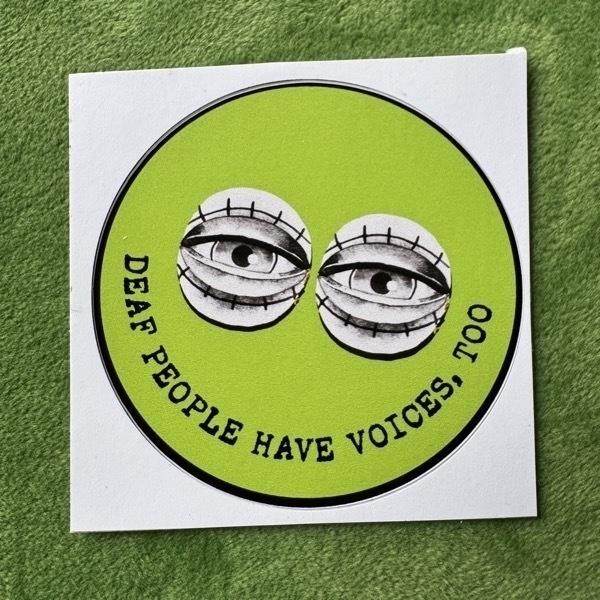 A green circular sticker with two illustrated eyes and with text DEAF PEOPLE HAVE VOICES, TOO.